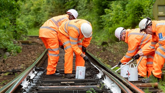 Engineers in orange high vis are painting railway tracks white to help keep them cool.