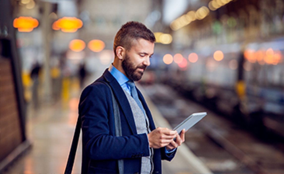 Man standing at a train station looking at his iPad