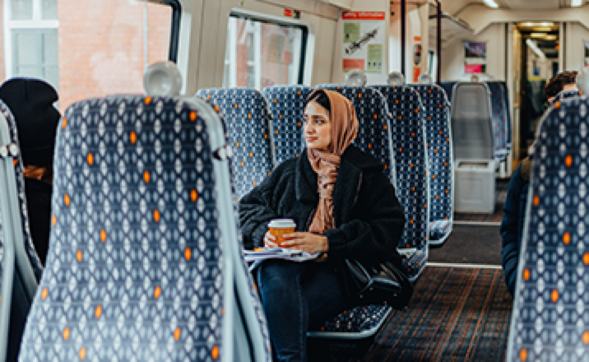 Woman sitting on an empty West Midlands Railway train enjoying a hot drink
